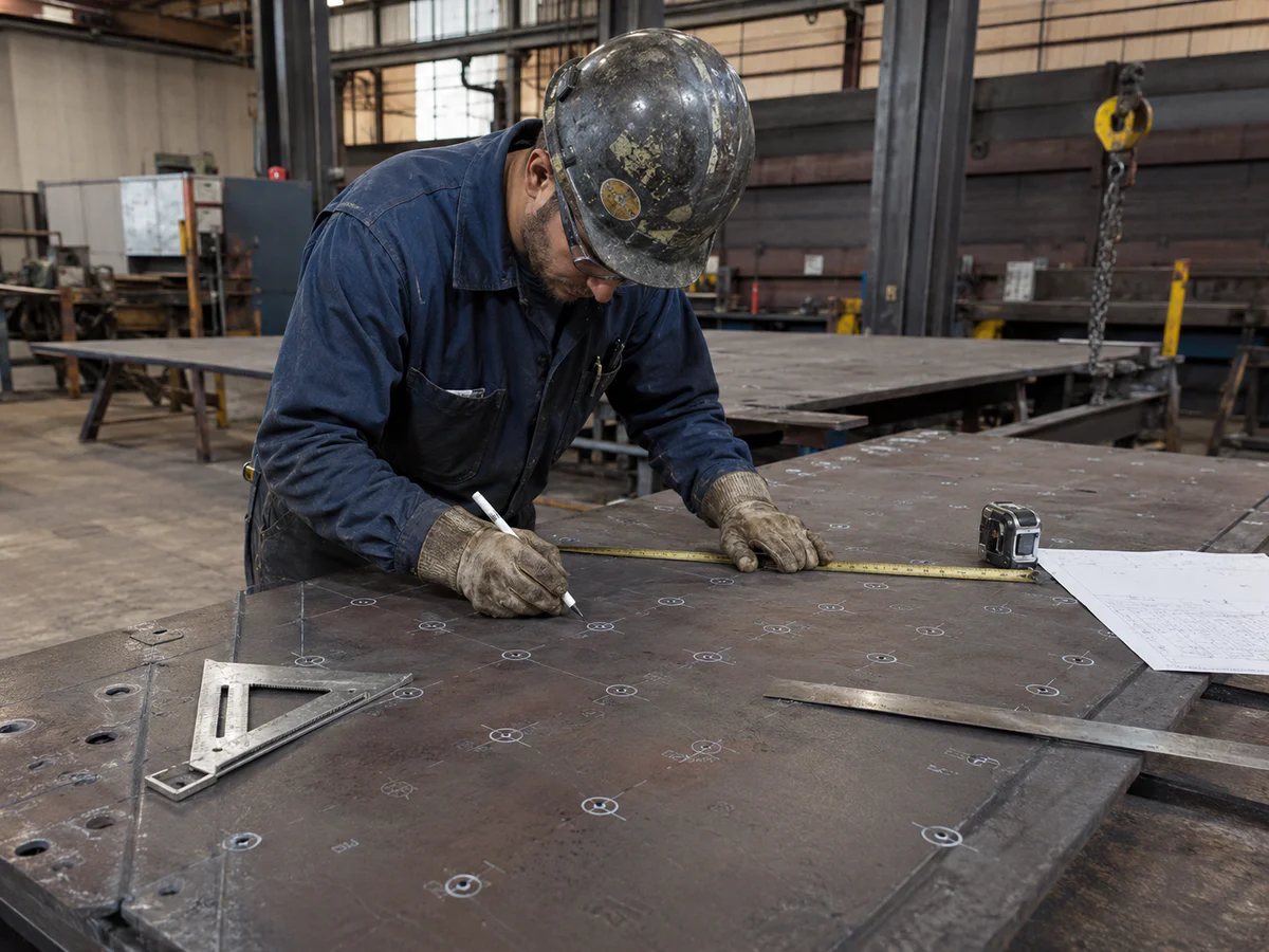 Worker marking hole positions on a steel plate by hand